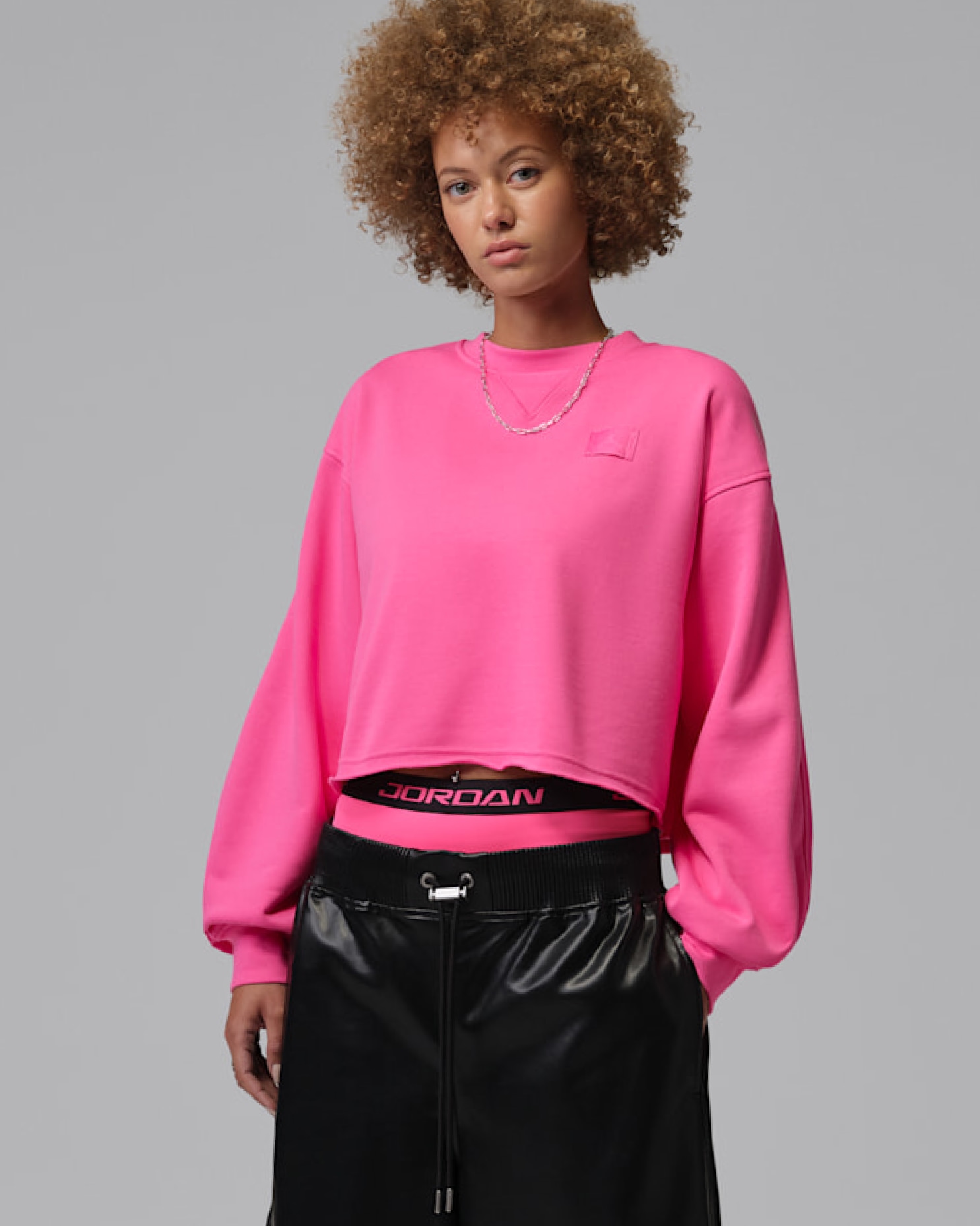 Model wearing pink cropped sweatshirt over black shorts with Jordan wordmark on elastic waistband