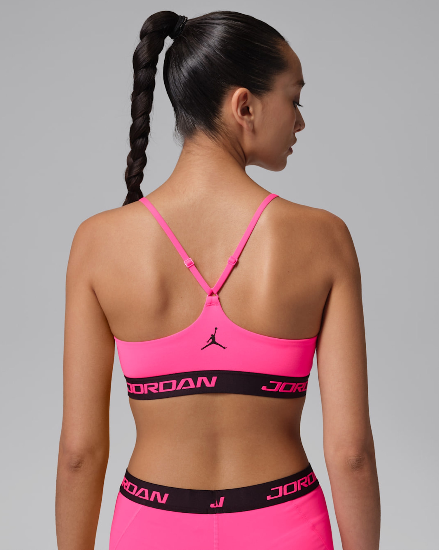 Rear view of model wearing pink Jordan sports bra with black wordmark trim and Jumpman logo