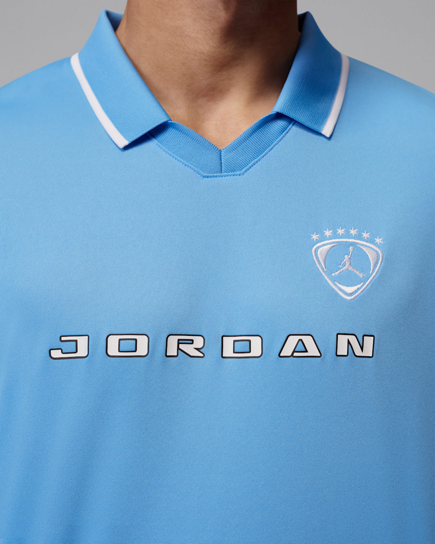 Close-up of light blue polo collar with white piping, Jordan wordmark, and star crest with Jumpman logo