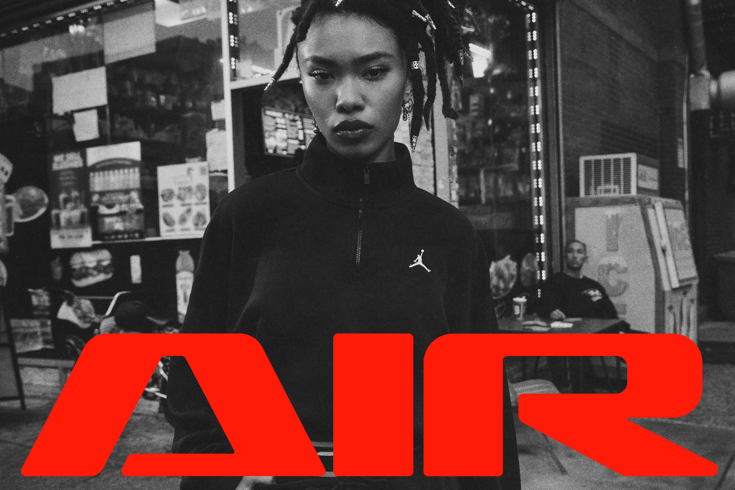 Black and white street photo of a woman in a black Jordan quarter-zip, with large red "Air" wordmark overlaid at bottom