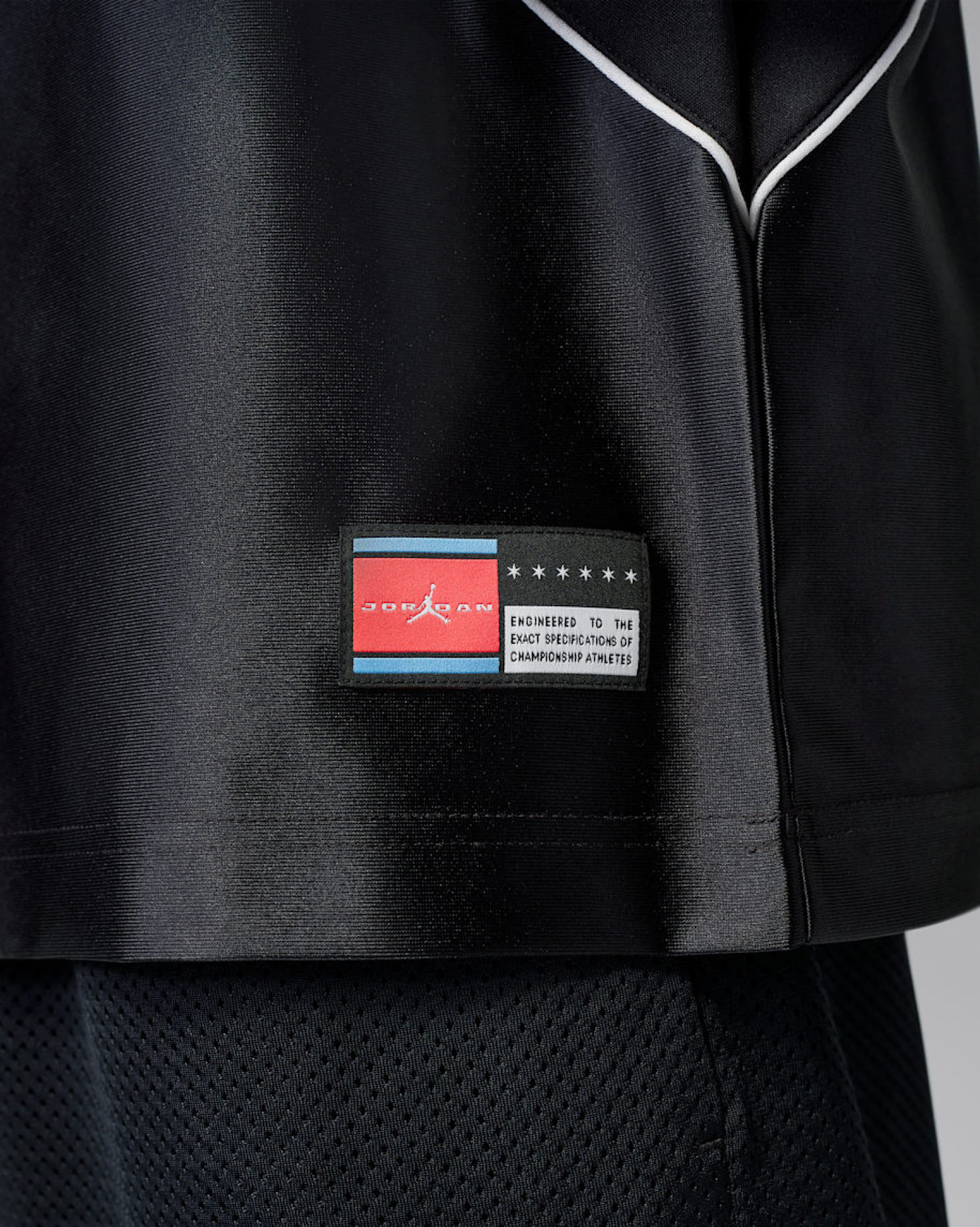 Close-up of black jersey hem showing woven Jordan flag tag and "Engineered to the exact specifications of championship athletes" label